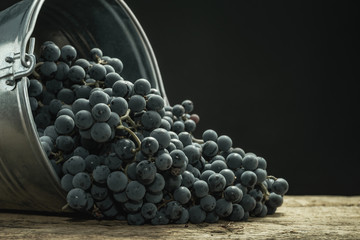 Poster - Beautiful wine grapes of silver basket on a old oak wooden table and black background.