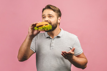 Wall Mural - Young man holding a piece of hamburger. Bearded gyu eats fast food. Burger is not helpful food. Very hungry guy. Diet concept. Isolated over pink background.