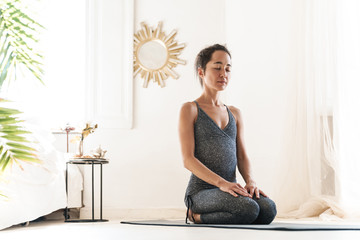 Sticker - Photo of concentrated sportswoman sitting on fitness mat and meditating while practicing yoga in bright room