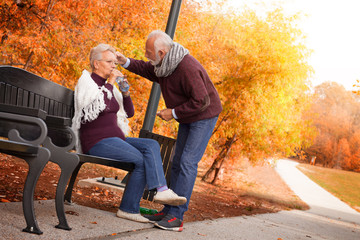 Grey haired husband helping health issue, supporting sick senior wife at park