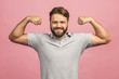 Waist-up portrait of muscular young man flexing his biceps against pink background.