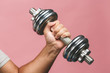 Close-up photo of man grabs a heavy dumbbell isolated over pink background with his hand. Concept lifting, fitness.