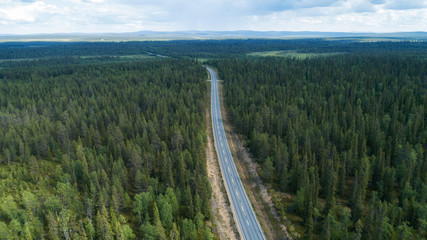 Wall Mural -  Aerial view from above of highway through the green summer forest in summer Lapland. Drone photography.