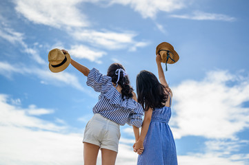 Two happy woman holding straw hat with hand raised to sky.