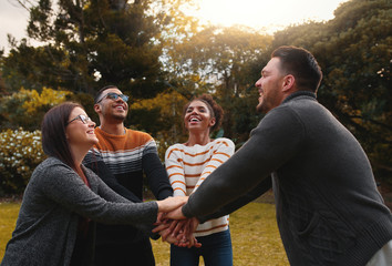 Poster - Group of happy multiethnic friends standing together in circle at park stacking their hands