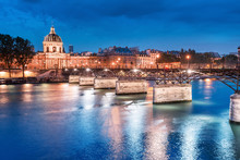Night Cityscape With Illuminated Academic Building Institut De France And Pedestrian Bridge With Lanterns Over The River Seine In Paris, France