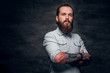 Groomed bearded man with tattooes is posing at dark photo studio.