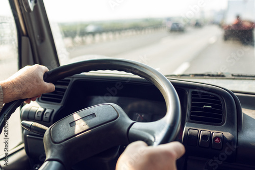 Fotografía Male driver hands are holding steering wheel of truck during the movement in the road
