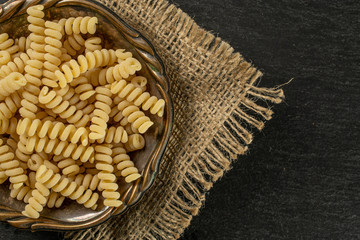 Lot of whole fresh raw pasta fusilli bucati in old iron bowl on jute cloth flatlay on grey stone