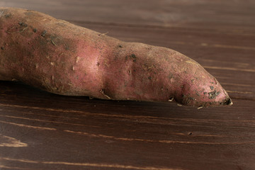 One whole fresh brown sweet potato on brown wood