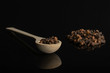 Lot of whole dry brown clove in a wooden spoon isolated on black glass