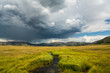 A stream winds through grasslands under a dramatic stormy sky in the Valles Caldera National Preserve, New Mexico