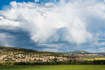 green fields contrasted with the red rock landscape of northern new mexico under a dramatic stormy s