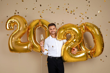 Wall Mural - Happy young man with glass of champagne near golden 2020 balloons on beige background. New Year celebration