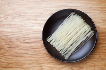 Wall Mural - Dried rice noodles in black plate on a wooden table. Top view.