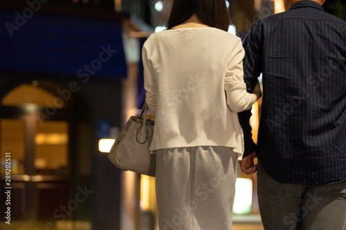 夜の繁華街で手を繋いで歩く男女の後ろ姿 Stock Photo Adobe Stock