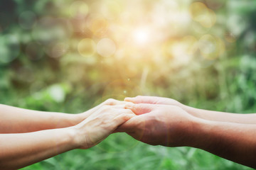 Wall Mural - Close up of Two people holding hand together over blurred green nature garden background, Business man and woman shaking hands, helping hand and teamwork  concept with copy space