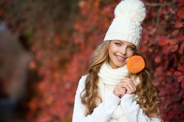 Wall Mural - Portrait of beautiful young woman walking outdoors in autumn. Girl with autumn yellow leaf in knitted hat and sweater.  Portrait of a girl with orthodontic appliance.