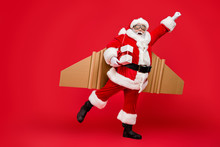 Full Length Profile Side Photo Of Crazy Funny Elderly Superhero Santa Start Launch Fly Up His Rocket Wings To Give Presents On Christmas Night Wear Costume Cap Hat Isolated Over Red Background