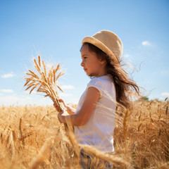 Wall Mural - Happy girl walking in golden wheat, enjoying the life in the field. Nature beauty, blue sky and field of wheat. Family outdoor lifestyle. Freedom concept. Cute little girl in summer field