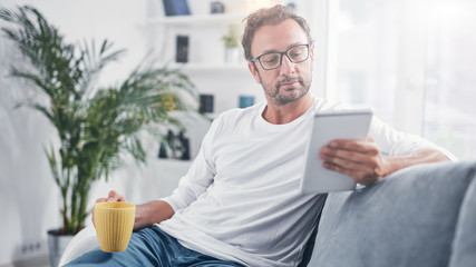 Wall Mural - Man holding tablet, surfing online and drinking coffee.