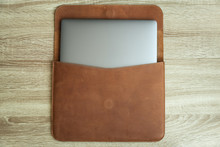 Brown leather case with laptop on wooden table. Top view. Copy space