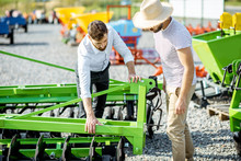 Young Agronomist With Salesman Or Manager At The Open Ground Of The Shop With Agricultural Machinery, Buying A New Plow For Tillage