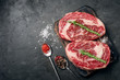 © Andrey - Two raw rib eye steak on the dark stone background prepared for cooking. Marbled beef top view