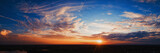 Fototapeta Zachód słońca - Wide panorama of sunset sky with clouds and sunlight over farm