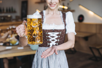 Wall Mural - cropped view of waitress in german national costume holding mug of light beer