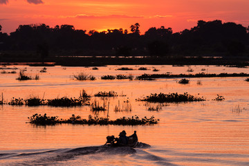 Wall Mural - Silhouette of fisherman to drive a boat on the lake at sunset scene