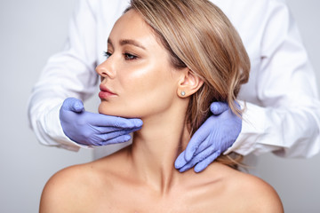 Close up portrait of young blonde woman with cosmetologyst hands in a gloves. Preparation for operation or procedure. Perfect skin, spa and care