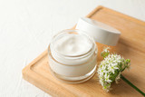 Fototapeta  - Jar with cream, allium flowers and board on white background, closeup