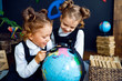 © ZaStock - Little twin girls in school uniform using magnifying glass to examine globe while sitting on floor during geography lesson