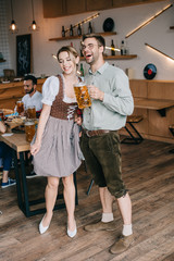 Wall Mural - young man and woman in traditional german costumes holding mugs of beer