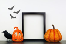 Mock Up Black Frame With Jack O Lantern, Pumpkin And Crow Decor On A Shelf Or Desk. Halloween Concept. Portrait Frame Against A White Wall With Bats.