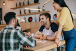 © LIGHTFIELD STUDIOS - young asian woman standing at wooden table near multicultural friends in pub
