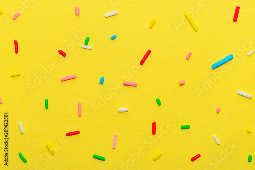 сlose up of colorful sprinkles over yellow background, decoration for festive...