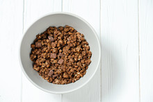 Top View On Fresh Chocolate Granola In Grey Bowl On White Wooden Background. Copy Space. Healthy And Tasty Breakfast. Vegan Food. Food Photo Background