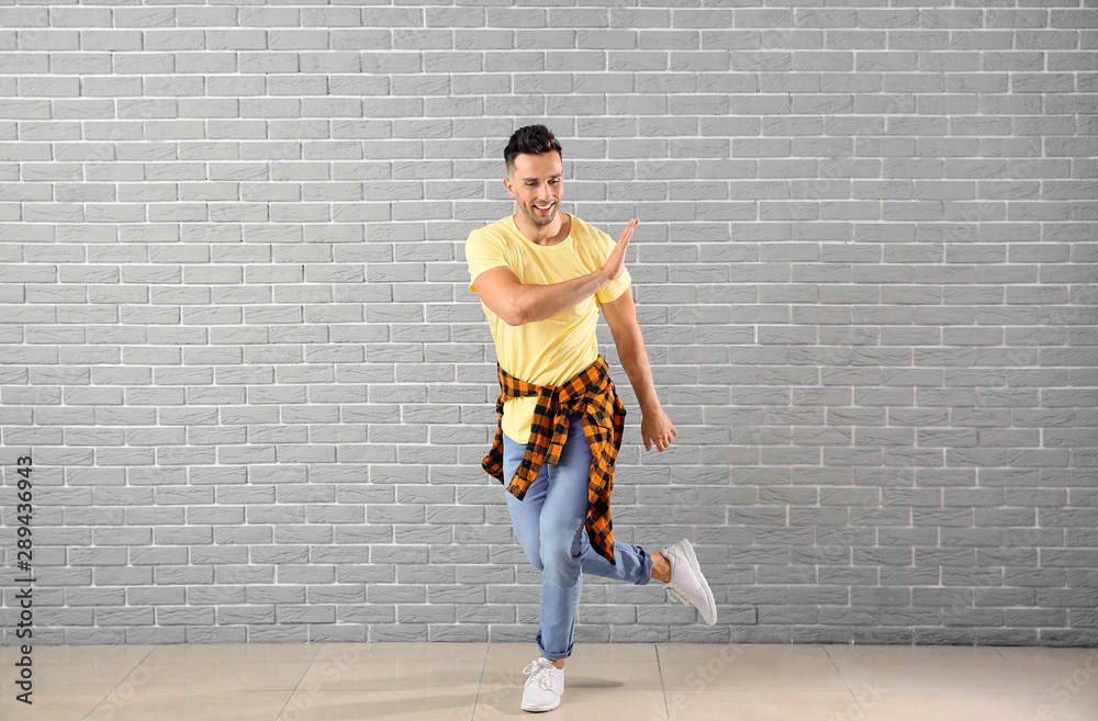 Handsome young man dancing against brick wall