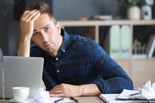 Fotomural Stressed young man at table in office