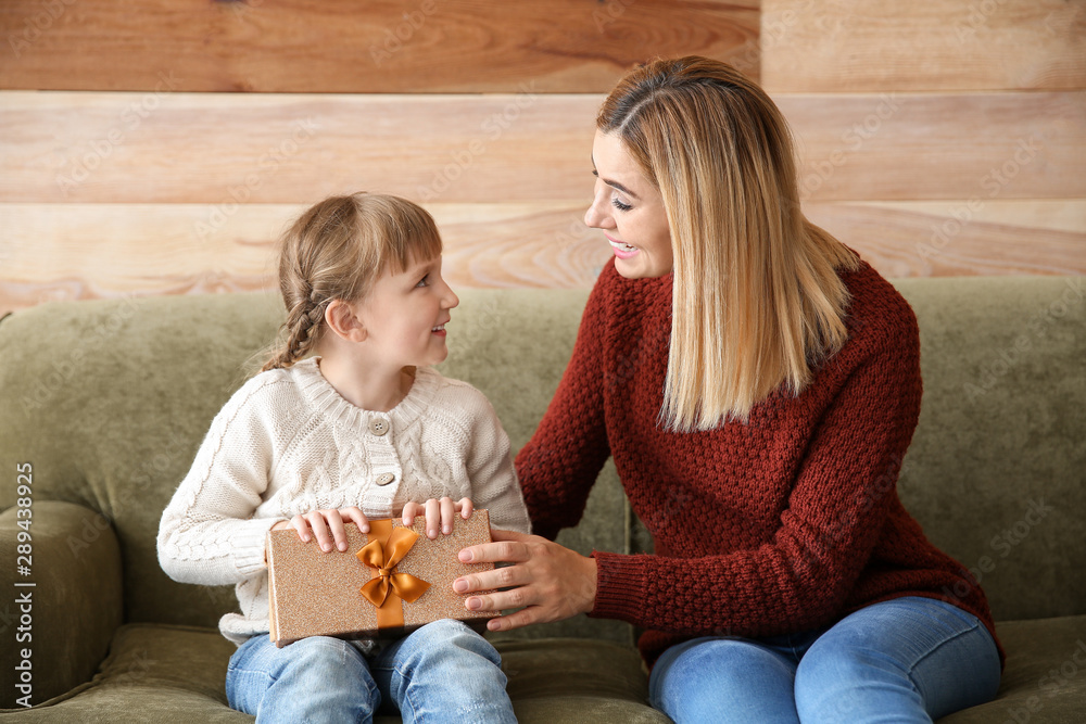 Happy mother and daughter with Christmas gift sitting on sofa