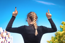 A young slender woman shows the middle finger with two hands, turning her back, the blue sky in the background. The girl sends everyone to fuck you symbol send you!