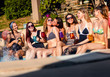 © Zoran Zeremski - Group of girlfriends at a poolside summer party sitting at the edge of a swimming pool drinking and having fun.