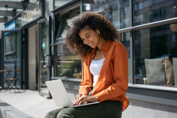 Successful freelancer typing on keyboard using laptop computer. Portrait of cheerful woman copywriter working project. Smiling African American student studying, learning language. Online education