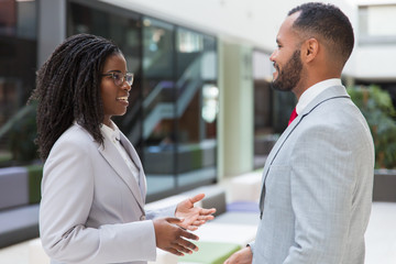 Happy friendly business partners discussing deal in office hall. Business man and woman standing in hallway, talking and gesturing. Partnership concept