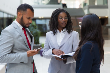 Successful diverse business people discussing contract in office hall. Business man and women standing in hallway, talking and reading document. Partnership concept