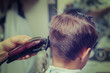 Barber shop. Barber making hairstyle to Caucasian boy using clipper.