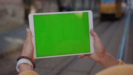 Close up hands woman using tablet device computer with green screen outdoors in street at sunlight background tram message pad technology chroma key female digital girl app chat finger slow motion