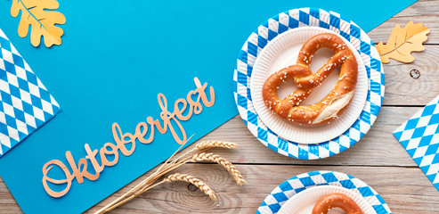 Wall Mural - Oktoberfest, flat lay on wooden table covered with blue paper and pretzels on blue white paper plates